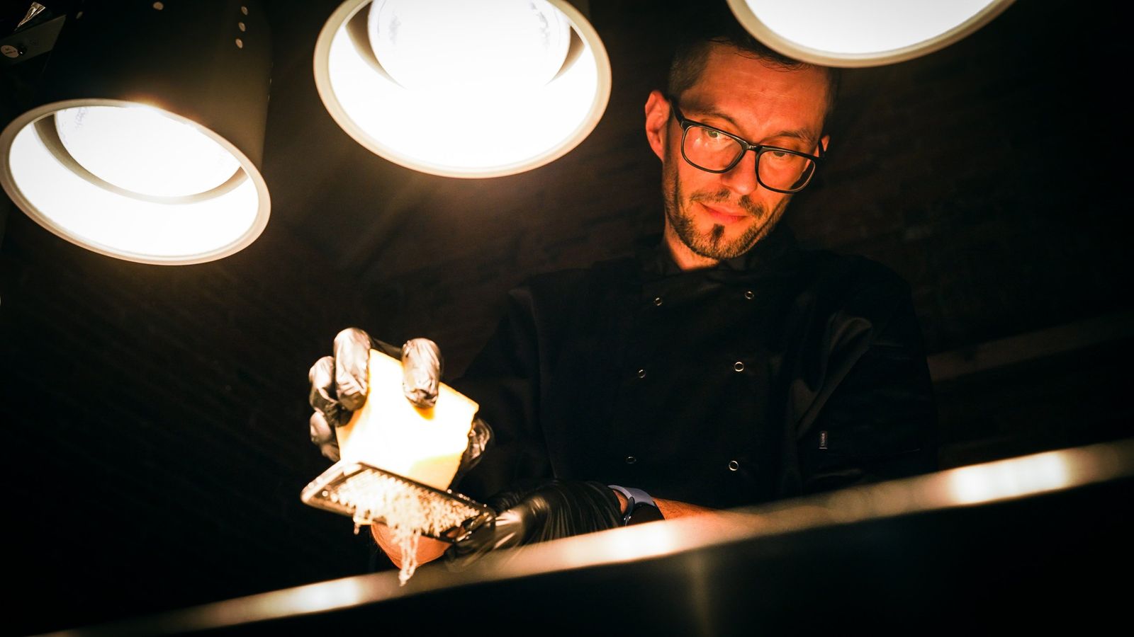 A chef grating hard cheese at the pass