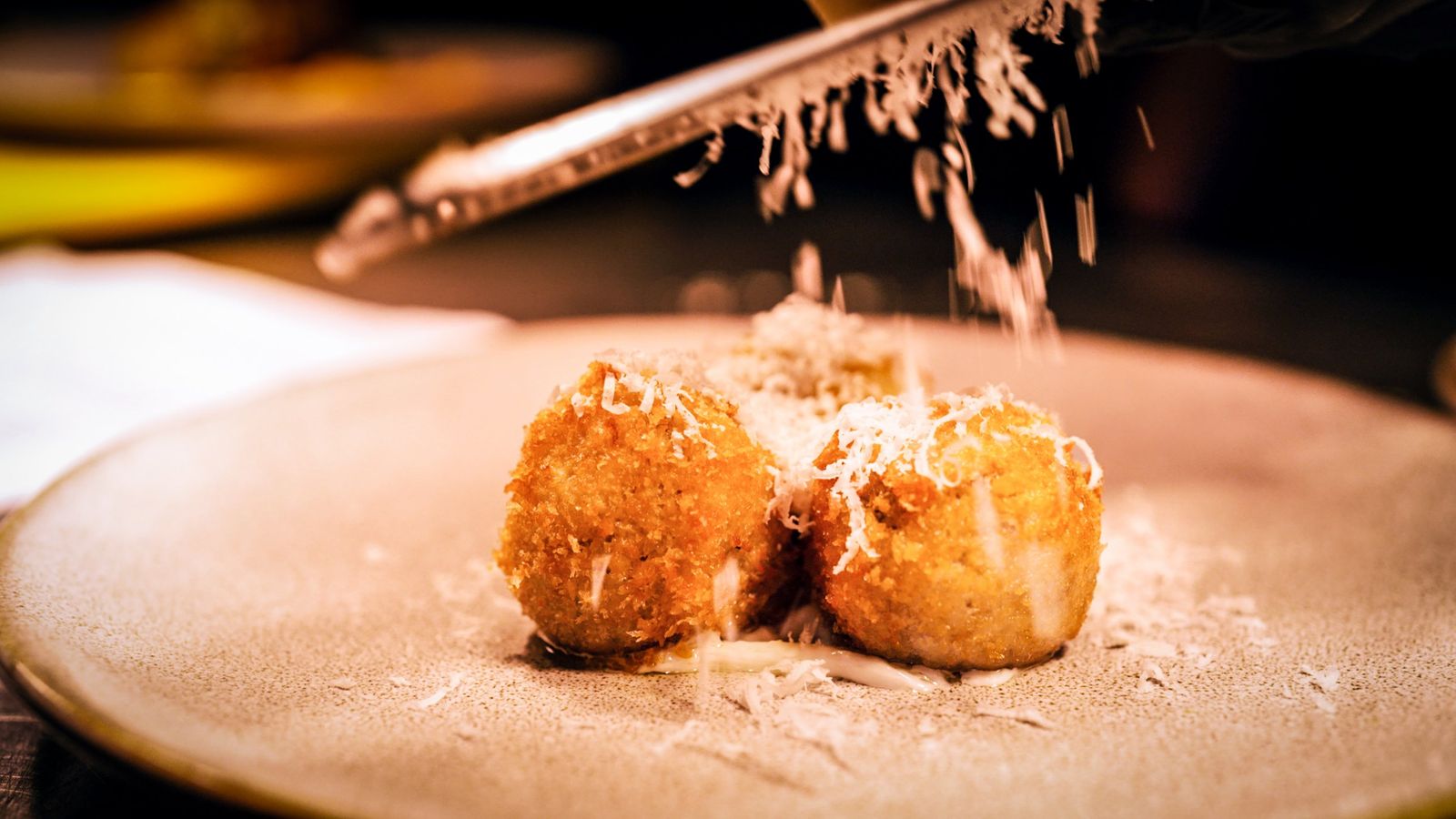 Cheese being grated over two golden croquettes